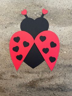 a red and black ladybug with hearts on it's back sitting on the ground