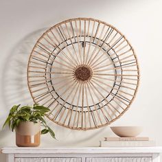 a white table topped with a plant and a rattan wall hanging on the wall