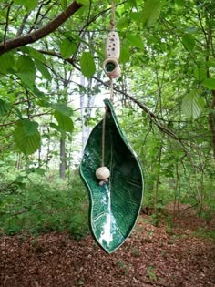 a green leaf shaped object hanging from a tree branch in the middle of a forest