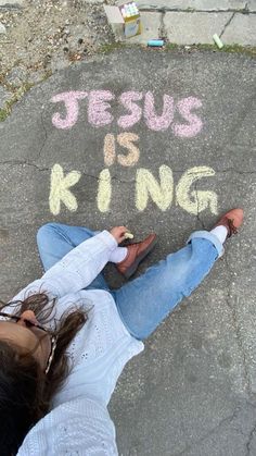 a woman laying on the ground drawing jesus is king with chalk in front of her