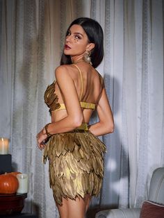 a woman in a gold dress standing next to a couch