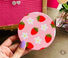 a person holding up a pink compact case with strawberries and daisies on it