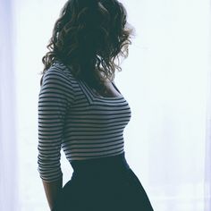 a woman standing in front of a window with her hands on her hips, wearing a striped shirt and black skirt