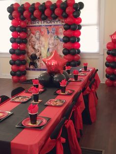 the table is set with black and red balloons, plates, cups, and napkins