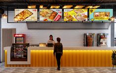 two people standing in front of a food court counter with menus on the wall