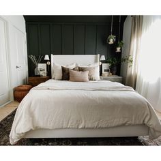 a bed with white linens and pillows in a dark colored room, next to a window