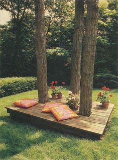 a wooden deck with pillows and potted plants on it in the middle of some trees