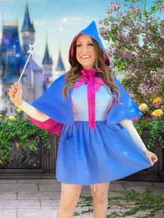 a woman in a blue dress and pink hoodie holding a wand with a castle in the background