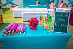 a blue table topped with lots of colorful umbrellas next to a sign that says shower some bubbles