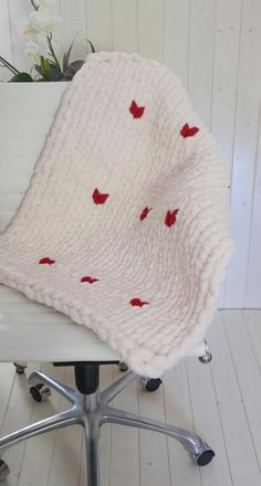 a chair with a blanket on top of it in front of a flower pot and white wall