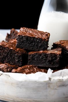 chocolate brownies with frosting in a white bowl next to a glass of milk