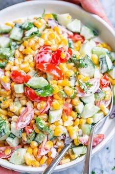 a white bowl filled with corn, cucumber and tomato salad on top of a marble table