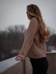 a woman with long hair leaning on a wall and looking over her shoulder at the sky