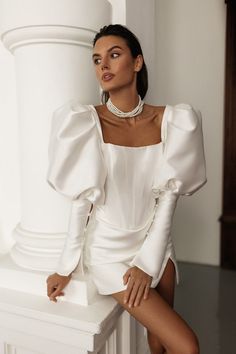 a woman sitting on top of a white counter next to a pillar wearing a necklace