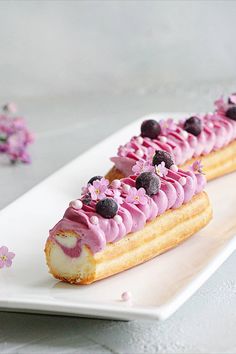 two desserts with pink icing and blueberries are on a white platter