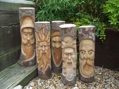 four carved wood faces are sitting on the ground in front of a wooden bench and some plants