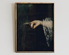 a painting hanging on the wall with a woman's hand holding something in it