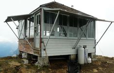 a small white house on top of a hill with a water heater in the foreground