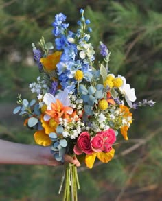 a bouquet of flowers being held by someone's hand with trees in the background