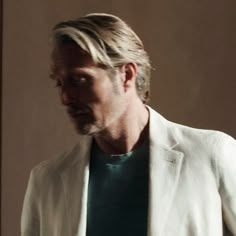 a man in a white jacket and green shirt looking down at his cell phone while standing next to a door