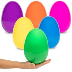 a hand holding an egg in front of five colored eggs