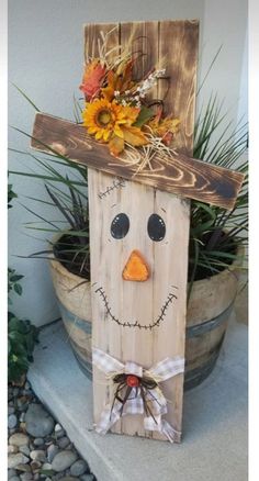 a wooden block with a scarecrow face and flowers on it's head, sitting next to a potted plant