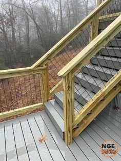 a wooden deck with stairs and railings in front of some trees on a foggy day