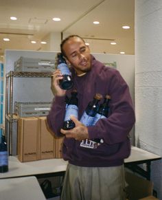 a man in a purple sweatshirt is talking on a cell phone and holding several bottles