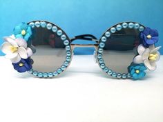 💙Cute blue flowery statment sunglasses 💙These fun vintage style sunglasses have silver frames with mirrored round  Lenses. They have been designed in an array of pretty blue large and small handmade flowers on the sides with a row of blue iredescent pearls round the rims. This particular style is nice and  lightweight to wear.  💙Great for festivals, carnivals, holidays and hen do's or for everyday wear to add a bit of fun to an outfit.  💙UV protection. 💙Exclusive design made by myself, you won't see any others made like these.  💙Other colours available in my shop or if you have an idea in mind please drop me a PM to discuss.  💙All my glasses come in a black pouch to keep them safe, please also handle with care as the flowers are delicate. 💙Checkout the full collection of Sunglasses Bohemian Sunglasses For Summer Parties, Bohemian Sunglasses With Gradient Lenses For Summer, Bohemian Summer Sunglasses With Gradient Lenses, Blue Sunglasses For Spring Party, Silver Sunglasses For Summer Parties, Handmade Sunglasses For Summer Parties, Light Blue Tinted Sunglasses For Spring, Silver Sunglasses With Mirrored Lenses For Spring, Silver Tinted Sunglasses For Spring