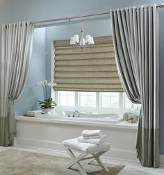 a white bath tub sitting next to a window covered in roman shades and drapes