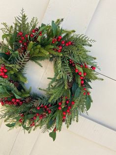 a green wreath with red berries and greenery on a white door frame hanging from the side of a building