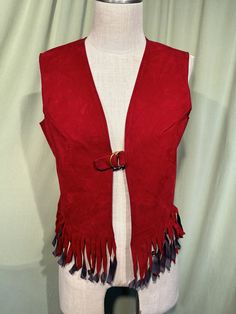 This is a cool vintage vest from the 1960s or so. Labeled Holiday of California.  No size tags. The bust measures 35" with the front edges touching. Would fit a larger bust worn open. Please see measurements below.  Made of a dark red faux suede. It is sleeveless with a fringed hem. It closes in the front with a slide buckle.  The vest is in very good condition. Show light wear & soil at the shoulder seams. Please see photos for details. Boho chic! If you have never worn vintage before, please measure yourself!! Vintage sizes run smaller than today's sizes, know your measurements before buying! Bust measured from side seam to side seam at the underarm: 17.5" for a 35" or slightly larger or smaller bust  Waist measured from side seam to side seam at the fringes: 16.5" for a 33" or a little Red Vest Women, Vintage Sleeveless Outerwear For Festivals, Fitted Sleeveless Outerwear For Festival, Fitted Red Outerwear For Festival, Fitted Retro Vest For Festivals, Red Vest For Fall Festival, Vintage Red Vest For Winter, Fitted Retro Red Vest, Fitted Red Retro Vest