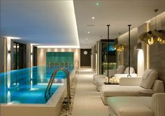 an indoor swimming pool with white couches and lights on the ceiling next to it