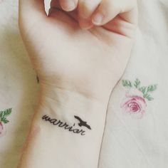 a person with a small tattoo on their wrist that reads, warrior and has roses around it