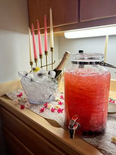 a table topped with a large jar filled with liquid and candles next to a bowl full of ice