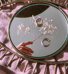 a person's hand holding a flower in front of a mirror with rings on it