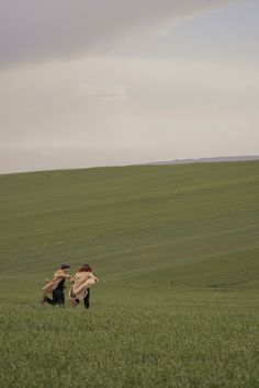 two people in a large field with one holding the other's back as they fly a kite