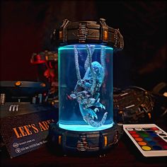 an illuminated lizard in a glass container on top of a table next to other items