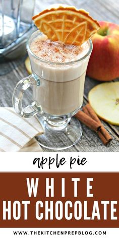 apple pie white hot chocolate in a glass mug with cinnamon on the rim and an apple next to it