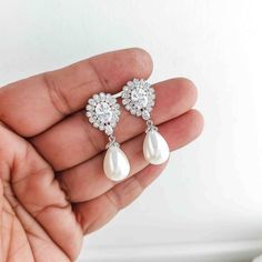 a hand holding a pair of earrings with pearls and diamonds on it, in front of a white background