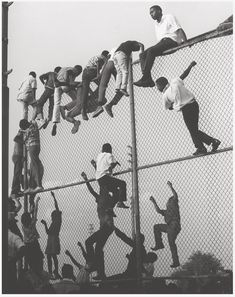 black and white photograph of people climbing up a fence