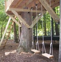 a tree house with swings and ladders attached to the side of it in the woods