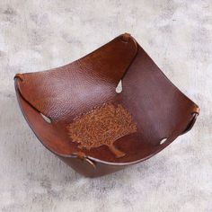 a brown leather bowl with a tree on the side and holes in the middle, sitting on a white surface