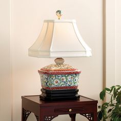 a lamp sitting on top of a wooden table next to a potted plant and vase