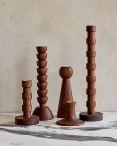 three wooden sculptures sitting next to each other on a marble counter top in front of a beige wall