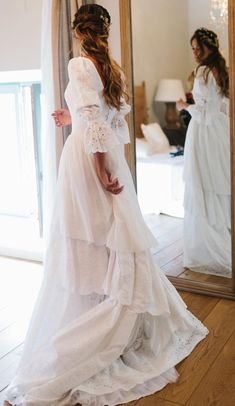 a woman standing in front of a mirror wearing a white dress