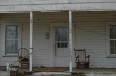 an old white house with rocking chairs on the porch