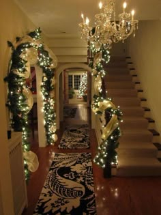 a hallway decorated for christmas with lights and garlands on the stairs, chandelier and rug