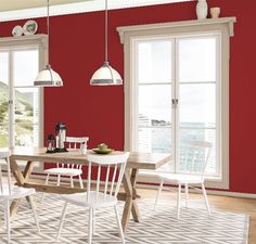 a dining room with red walls and white chairs in front of a table that is surrounded by windows