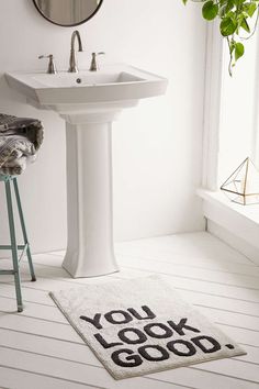 a bathroom with a rug that says you look good next to a sink and stool